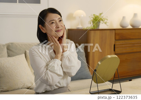 夜のリビングで顔に化粧水を塗る50代の女性 122373635