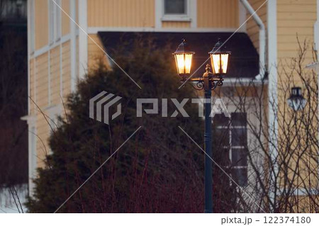 A lit street lamp by a cozy house adds warmth, charm, and elegance to the evening 122374180