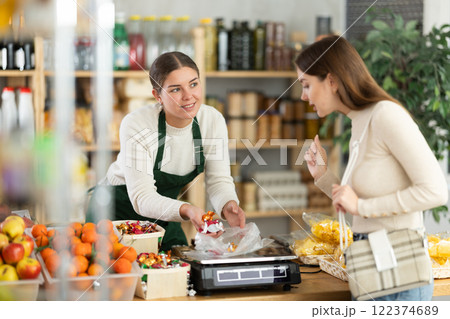 Female vendor weighs candies on scales and sells candies to customer 122374689