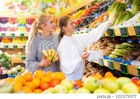 Positive woman and teenage girl shopping vegetables and fruits at grocery shop Positive woman and teenage girl shopping vegetables and fruits at grocery shop 122375077