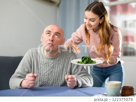 Portrait of a disgruntled man, to whom a young woman brought a plate of spinach 122375079