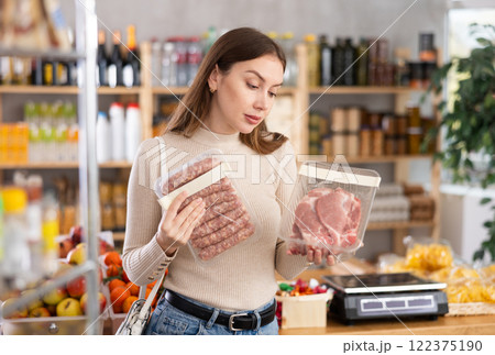 Young woman choosing raw sausages and pork in grocery store 122375190