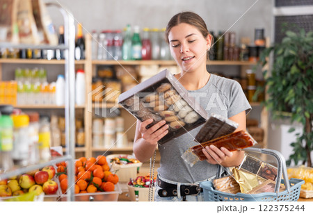 Grocery shopping at supermarket - girl chooses sweets, nougat, cookies and candies 122375244