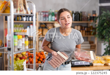 Female shopper chooses between raw sausages and pork in grocery supermarket 122375245