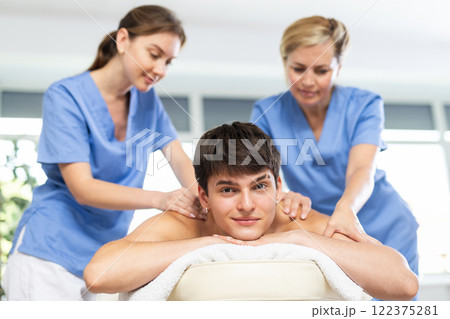 Two female masseurs massaging a man in spa complex Two female masseurs massaging a man in spa complex 122375281