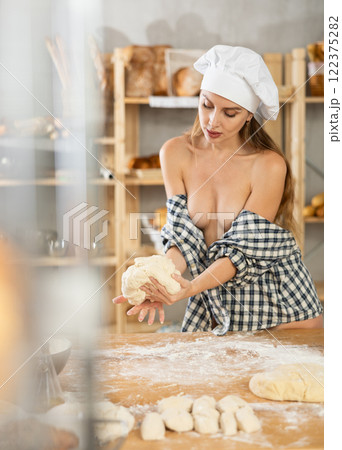 Woman in plaid shirt over bare body kneading dough in bakery 122375282