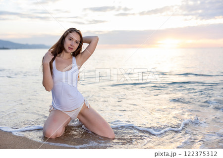 Young woman standing on knees on sand on beach, posing artistically 122375312