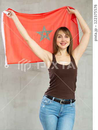 Happy young woman holding flag of Morocco against unicoloured background 122375576