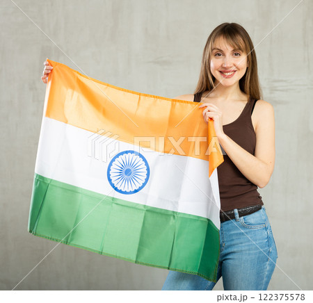Happy young woman holding flag of India against unicoloured background Happy young woman holding flag of India against unicoloured background 122375578