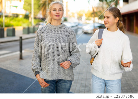 Happy mom and teen daughter walk along street of European autumn city 122375596