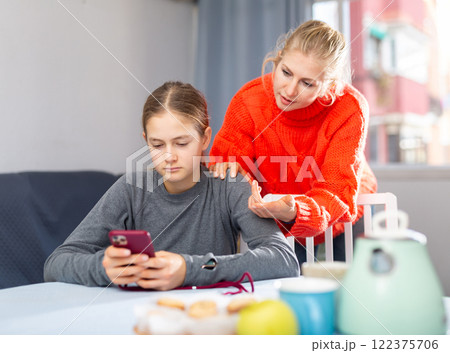 Daughter plays on smartphone while mother tries to talk to her Daughter plays on smartphone while mother tries to talk to her 122375706