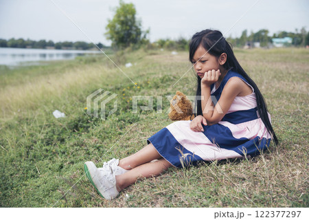 Sad girl hugging teddy bear sadness alone in green garden park. Lonely girl feeling sad unhappy sitting outdoors with best friend toy. Autism child play teddy bear best friend. Family violence concept 122377297