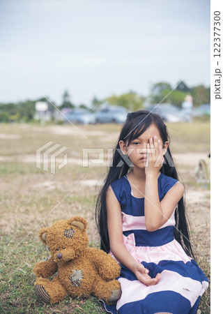 Sad girl hugging teddy bear sadness alone in green garden park. Lonely girl feeling sad unhappy sitting outdoors with best friend toy. Autism child play teddy bear best friend. Family violence concept 122377300