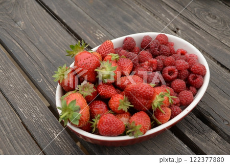 raspberries and strawberries, red berries, in a plate on a dark wooden background 122377880