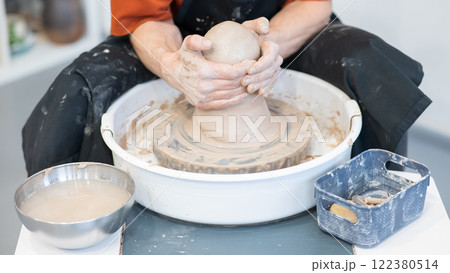 The potter kneads the clay before using it on the potter's wheel. Close-up of a man's hands. The potter kneads the clay before using it on the potter's wheel. Close-up of a man's hands. 122380514