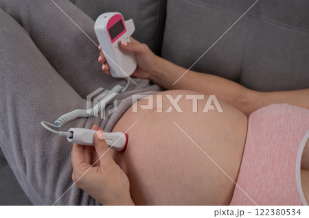 Close-up of a pregnant woman's belly using a home doppler. Normal baby heartbeat. 122380534