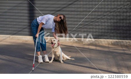 A blind woman walks her guide dog on the street. Girl hugging a labrador.  122380559