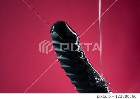 Lube pouring on black dildo on pink background. Lube pouring on black dildo on pink background. 122380560