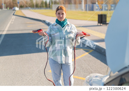 Woman holding clamps for charging a car battery. Woman holding clamps for charging a car battery. 122380624