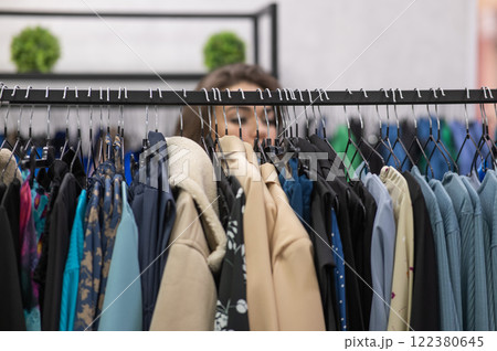 Portrait of a fat woman in a plus size store through hangers with clothes.  122380645