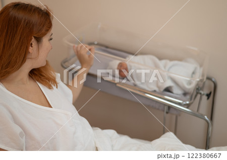 A young mother admires her newborn son in the maternity hospital.  122380667