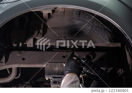 An auto mechanic applies anti-corrosion mastic to the underbody of a car. An auto mechanic applies anti-corrosion mastic to the underbody of a car. 122380801