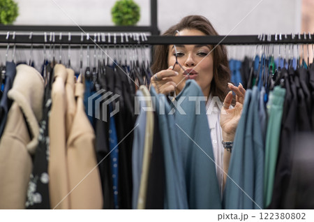 Portrait of a fat woman in a plus size store through hangers with clothes. Portrait of a fat woman in a plus size store through hangers with clothes. 122380802