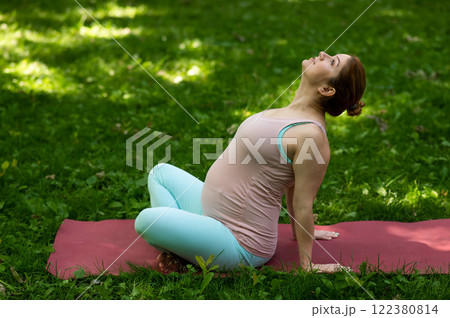 Pregnant caucasian woman doing yoga in the park.  122380814