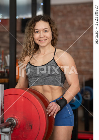 Caucasian forty year old woman putting a weight plate on a barbell in the gym. Vertical photo. Caucasian forty year old woman putting a weight plate on a barbell in the gym. Vertical photo. 122380827