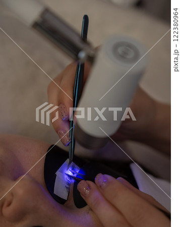 A woman undergoing eyelash extension procedure using an ultraviolet lamp. A woman undergoing eyelash extension procedure using an ultraviolet lamp. 122380964
