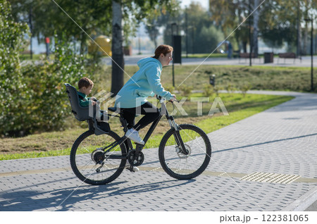 Caucasian woman riding a bicycle with her toddler son sitting behind her in a child seat. Caucasian woman riding a bicycle with her toddler son sitting behind her in a child seat. 122381065