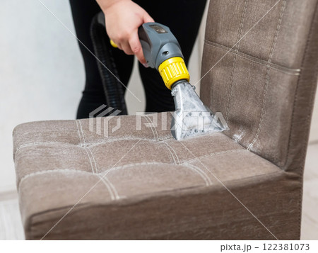 Woman cleaning a fabric chair with a professional washing vacuum cleaner. Woman cleaning a fabric chair with a professional washing vacuum cleaner. 122381073