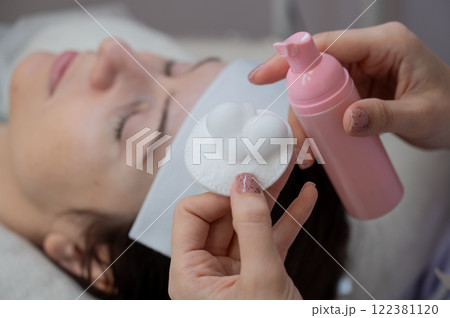 A professional applies cleansing foam to a cotton pad in a beauty salon.  122381120