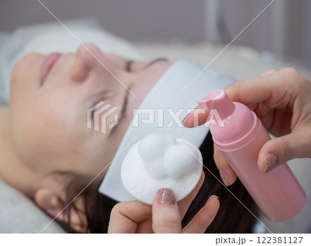 A professional applies cleansing foam to a cotton pad in a beauty salon.  A professional applies cleansing foam to a cotton pad in a beauty salon.  122381127