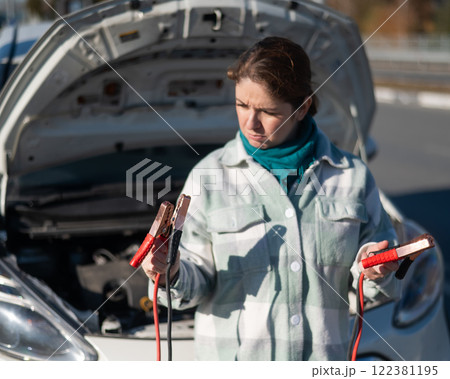 Woman holding clamps for charging a car battery. Woman holding clamps for charging a car battery. 122381195