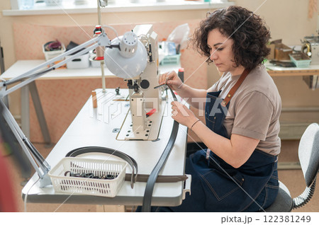 A woman tanner sews a leather belt on a sewing machine.  122381249