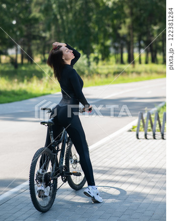 Rear view of Caucasian woman riding bike in park. Vertical photo.  122381284