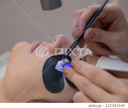 A woman undergoing eyelash extension procedure using an ultraviolet lamp. A woman undergoing eyelash extension procedure using an ultraviolet lamp. 122381348