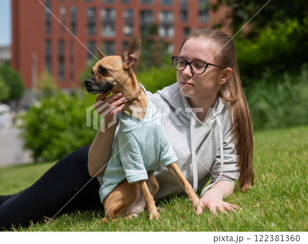 Young Caucasian woman lying on the lawn while walking with a small dog. Young Caucasian woman lying on the lawn while walking with a small dog. 122381360