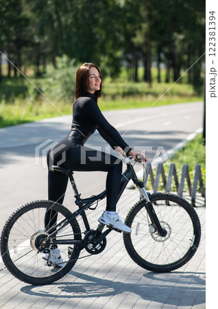 Rear view of Caucasian woman riding bike in park. Vertical photo.  122381394