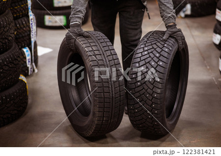 Mechanic keeps new summer and winter car tires in the garage. Comparison of wheels for different seasons. Mechanic keeps new summer and winter car tires in the garage. Comparison of wheels for different seasons. 122381421