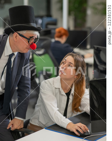 Caucasian woman communicates with an elderly man in a clown costume in the office. Vertical photo.  122381531