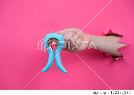 Female hand sticking out of pink paper background with blue curved vibrator sex toy.  122381580