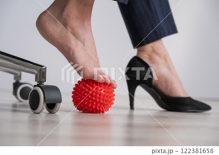 Business woman massages her feet on a massage ball with spikes. 122381658
