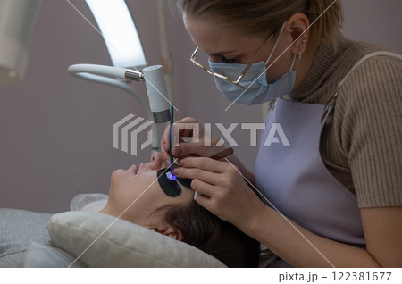 A woman undergoing eyelash extension procedure using an ultraviolet lamp. A woman undergoing eyelash extension procedure using an ultraviolet lamp. 122381677