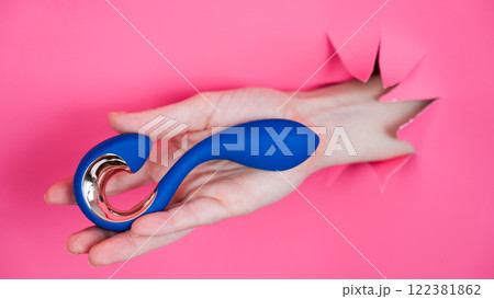 Hand with blue vibrator sticking out through pink paper background.  122381862