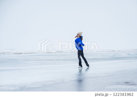 Caucasian woman in a blue sweater is skating on a frozen lake. The figure skater performs the program. Caucasian woman in a blue sweater is skating on a frozen lake. The figure skater performs the program. 122381962