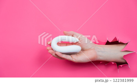 Female hand sticking out with white sex toy through pink paper background. Copy space.  122381999
