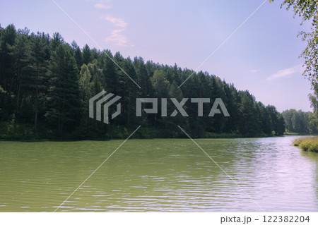 Picturesque view of a forest lake with clear water reflecting green trees and blue sky. The shore is covered with dense coniferous and deciduous trees. Film photography effect and grunge effect Picturesque view of a forest lake with clear water reflecting green trees and blue sky. The shore is covered with dense coniferous and deciduous trees. Film photography effect and grunge effect 122382204