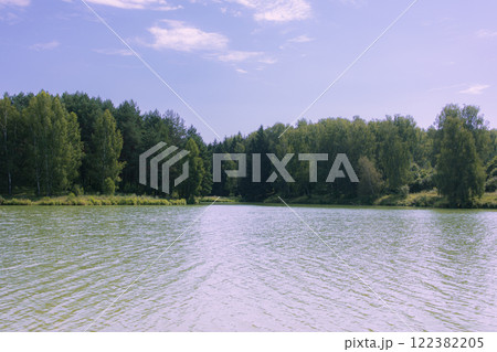 Picturesque view of a forest lake with clear water reflecting green trees and blue sky. The shore is covered with dense coniferous and deciduous trees. Film photography effect and grunge effect Picturesque view of a forest lake with clear water reflecting green trees and blue sky. The shore is covered with dense coniferous and deciduous trees. Film photography effect and grunge effect 122382205